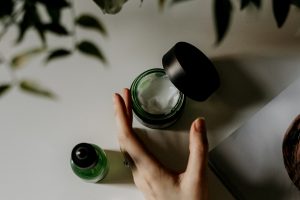 holding a small green bottle of face cream